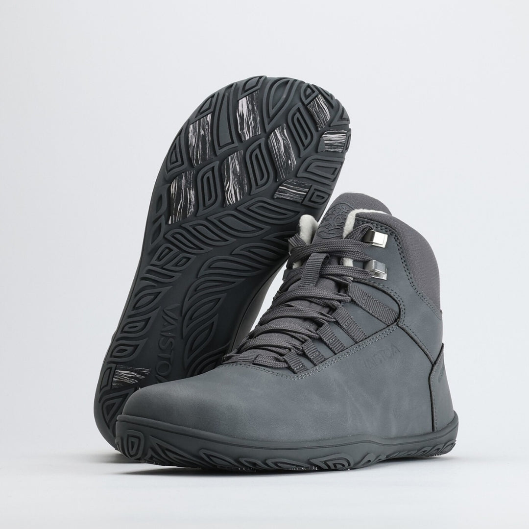 Pakkasharmaa Vaistoa Uoma Talvi 3 -paljasjalkavaelluskenkäpari, jossa toinen kenkä nojaa toiseen ja pohjan kitkapalat näkyvät. Kuvan päällä näkyy Design from Finland -merkintä.