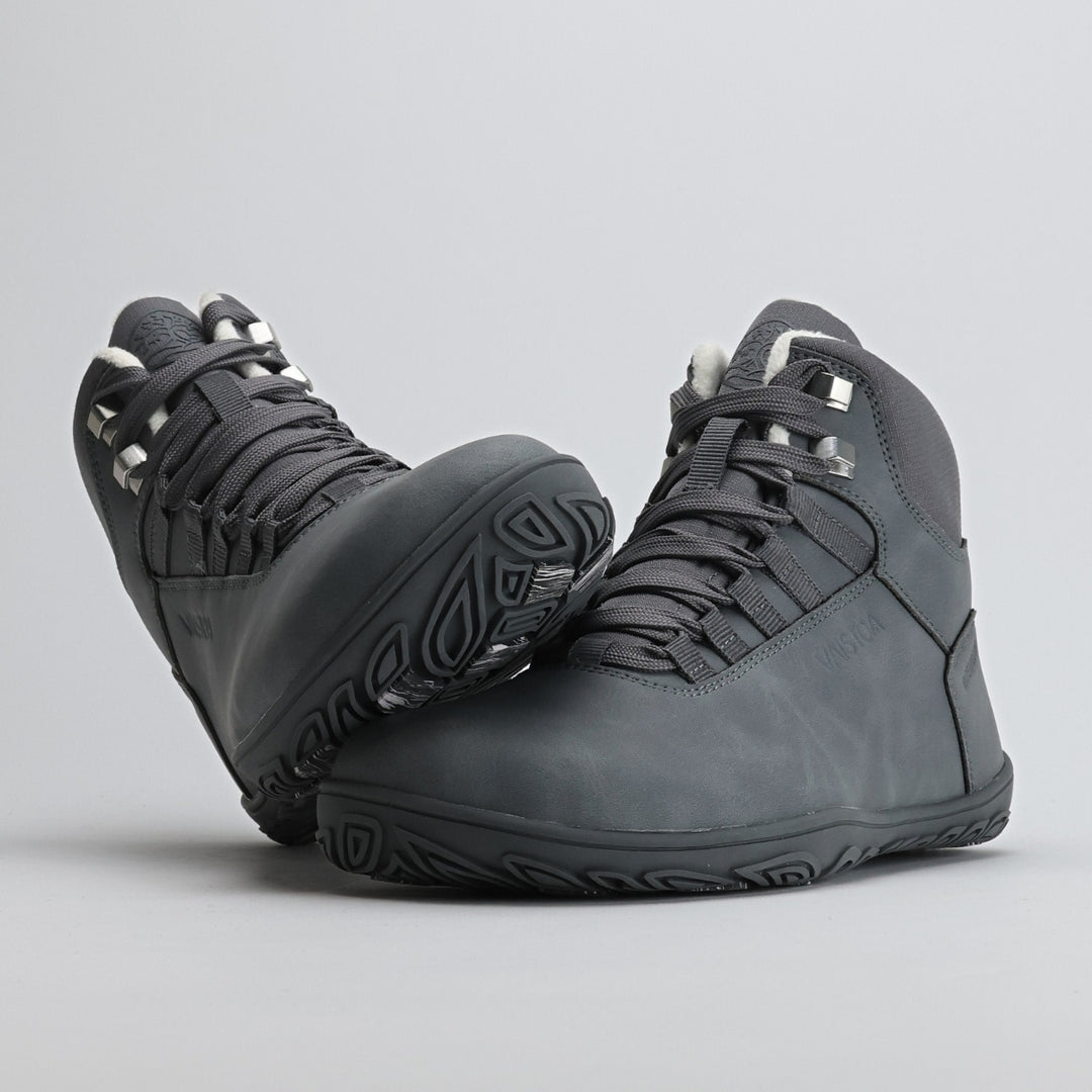 Pakkasharmaa Vaistoa Uoma Talvi 3 -kenkäpari, jossa toinen kenkä nojaa toisen varvastilaan. Kuvassa näkyy leveä varvastila ja pitävä pohjakuviointi.