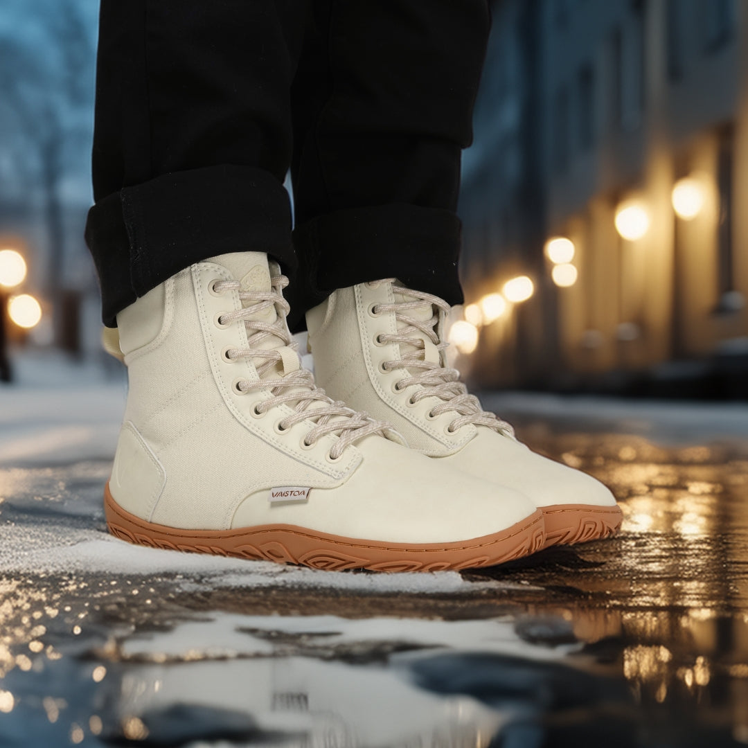 Luonnonvalkeat Vaistoa Hurmos 2 -paljasjalkamaiharit käytössä iltavalaistussa kaupunkiympäristössä. Henkilö seisoo märällä lumella katuvalojen loisteessa.