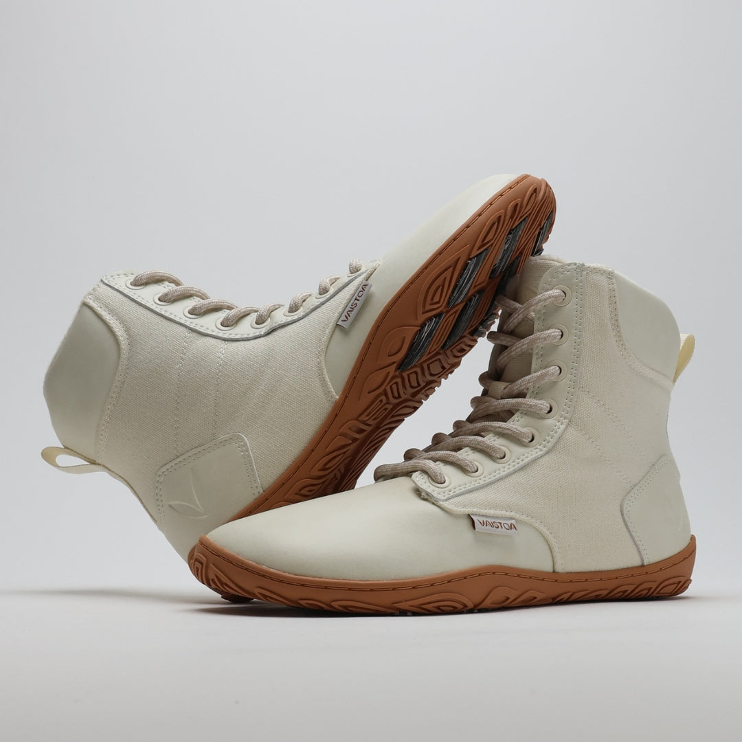 Luonnonvalkea Vaistoa Hurmos 2 -paljasjalkamaiharipari kuvattuna siten, että toinen kenkä nojaa toiseen ja paljastaa ruskean pohjan kitkapalat. Kuvakulma korostaa kevyttä rakennetta ja talvipitoa.