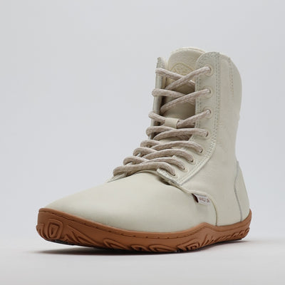 Luonnonvalkea Vaistoa Hurmos 2 -paljasjalkamaihari kuvattuna etuviistosta. Korkea varsi, ruskea ohut pohja ja vaalea nauhoitus korostavat kevyttä ja minimalistista talvimuotoilua.