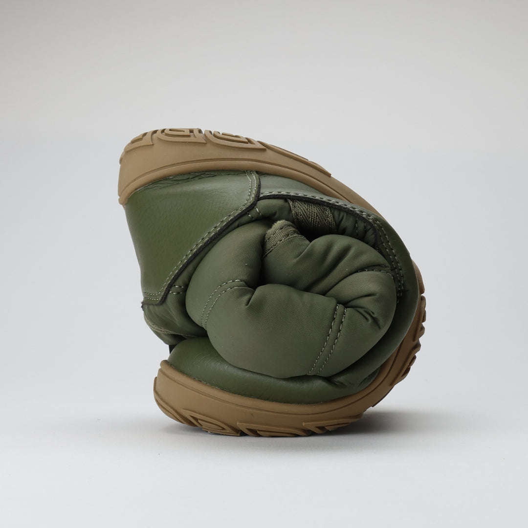 Vaistoa Hanki – korkeavartiset paljasjalkakengät talveen, väri oliivinvihreä. Kuvassa kenkä rullattuna, korostaen ohuen ja joustavan pohjan rakennetta, joka mahdollistaa jalan luonnollisen liikkeen ja tuntuman maahan.