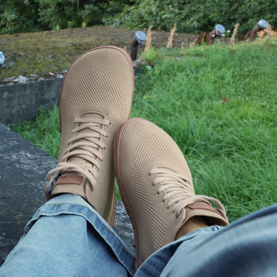 Vaistoa Iloa Mid latte – korkeavartiset paljasjalkatennarit farkkujen kanssa; kuvattuna ylhäältä istuma-asennossa korostaen kengän leveää varvastilaa, hengittävää neulepintaa ja tasaista, taipuisaa pohjaa ilman kantakorkoa luonnolliseen liikkumiseen.