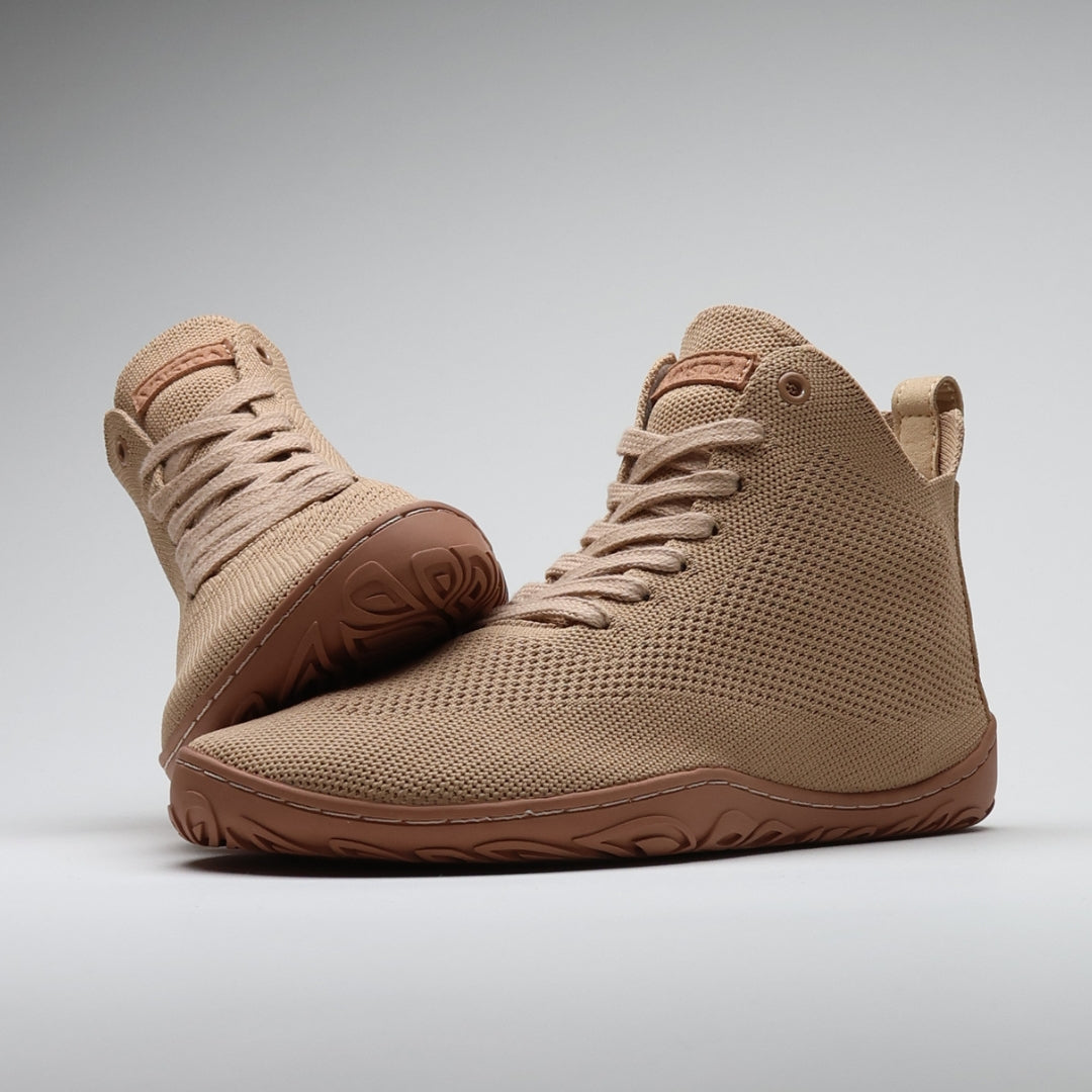 Vaistoa Iloa Mid latte – korkeavartiset paljasjalkatennarit tyylikkäästi aseteltuna pohjaa vasten: etualalla kenkä sivuviistossa, taustalla toinen kenkä pohja esillä. Leveä jalanmuotoinen varvastila sekä ohut, joustava tasapohja ilman kantakorkoa tukevat luonnollista liikkumista.