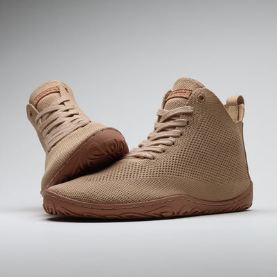 Vaistoa Iloa Mid latte – korkeavartiset paljasjalkatennarit tyylikkäästi aseteltuna pohjaa vasten: etualalla kenkä sivuviistossa, taustalla toinen kenkä pohja esillä. Leveä jalanmuotoinen varvastila sekä ohut, joustava tasapohja ilman kantakorkoa tukevat luonnollista liikkumista.