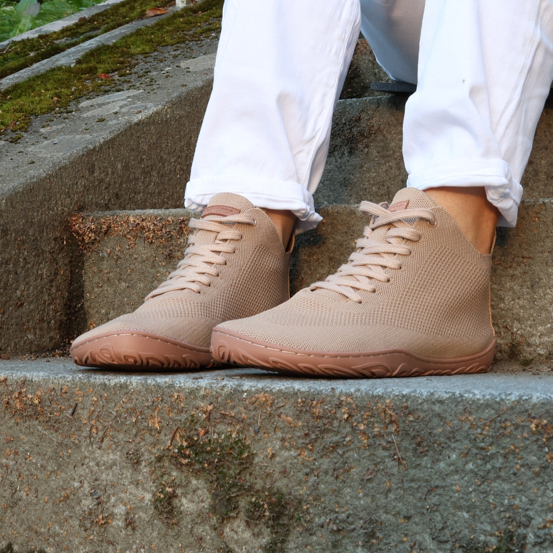 Vaistoa Iloa Mid latte – korkeavartiset paljasjalkatennarit valkoisten farkkujen kanssa; kuvattuna portailla, korostaen kengän hengittävää neulepintaa, leveää varvastilaa ja tasaista, joustavaa pohjaa ilman kantakorkoa luonnolliseen kävelyyn.