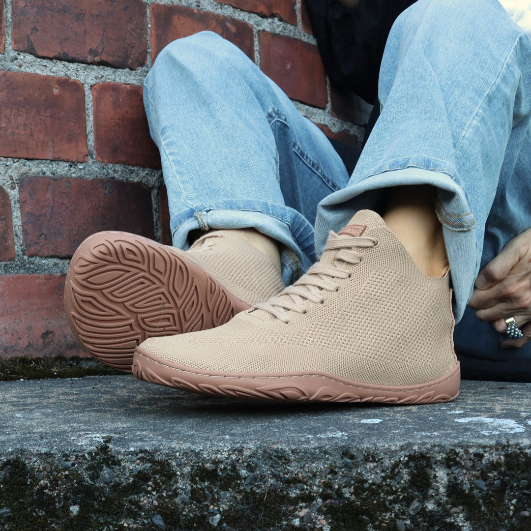 Vaistoa Iloa Mid latte – korkeavartiset paljasjalkatennarit käytössä ulkona vaaleansinisissä farkuissa; hengittävä neulekangas, leveä varvastila ja tasainen, taipuisa pohja ilman kantakorkoa tukevat luonnollista liikkumista.