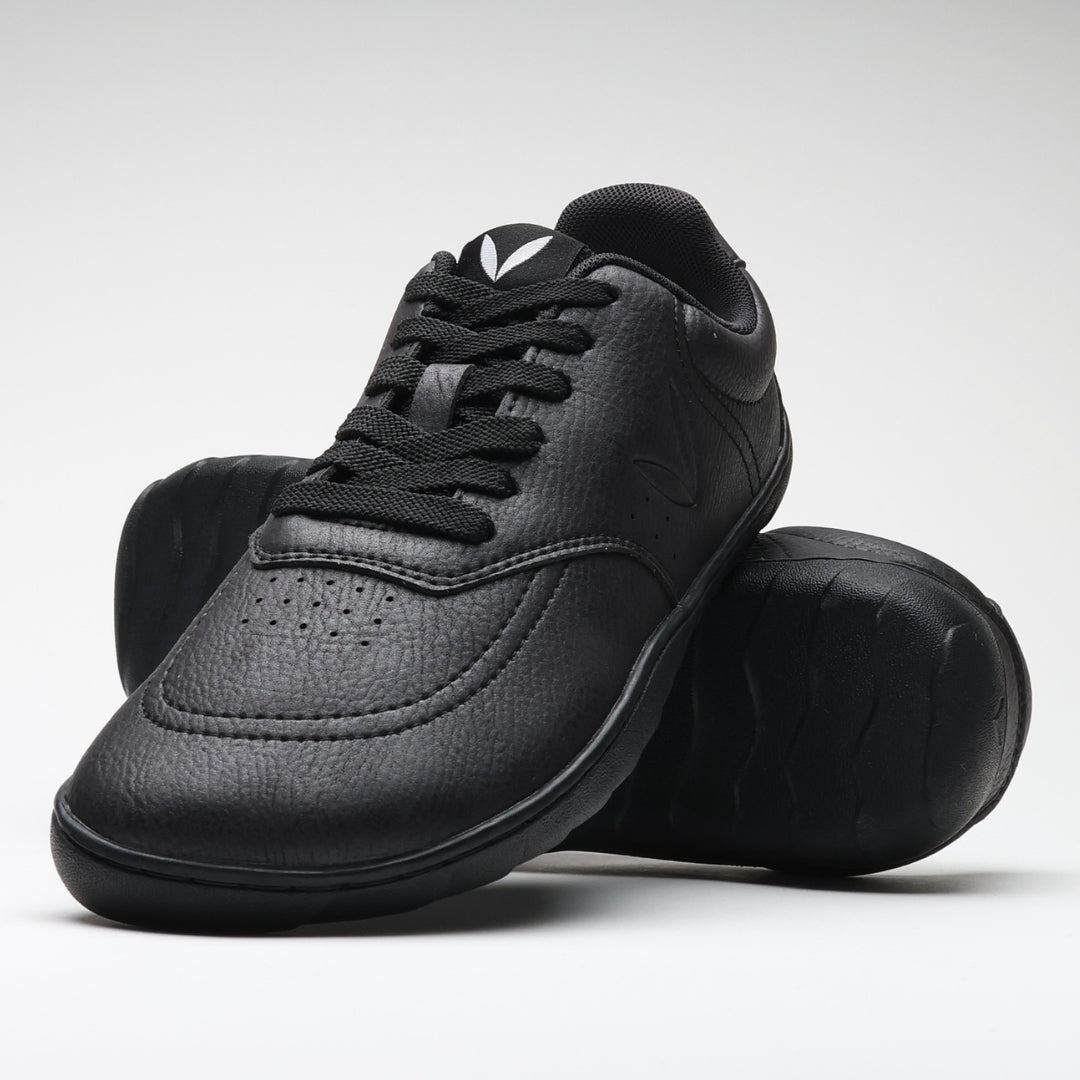 Vaistoa Katu 2 mustat paljasjalkasneakerit – tyylikkäästi aseteltuna niin, että toinen kenkä nojaa toisen pohjaa vasten, korostaen minimalistista muotoilua ja ohuen pohjan joustavuutta.