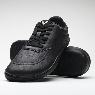 Vaistoa Katu 2 mustat paljasjalkasneakerit – tyylikkäästi aseteltuna niin, että toinen kenkä nojaa toisen pohjaa vasten, korostaen minimalistista muotoilua ja ohuen pohjan joustavuutta.