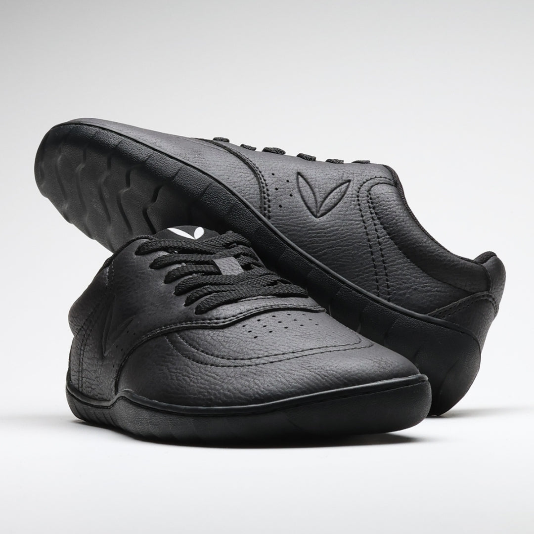 Vaistoa Katu 2 mustat paljasjalkasneakerit – tyylikkäästi aseteltuna niin, että toinen kenkä lepää toisen päällä, korostaen minimalistista muotoilua ja siroa siluettia.