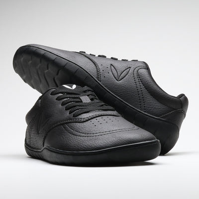 Vaistoa Katu 2 mustat paljasjalkasneakerit – tyylikkäästi aseteltuna niin, että toinen kenkä lepää toisen päällä, korostaen minimalistista muotoilua ja siroa siluettia.