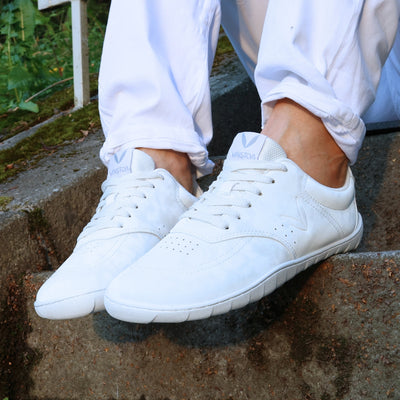 Vaistoa Katu 2 valkoiset paljasjalkasneakerit käytössä – henkilö seisoo ulkona portailla kesäpäivänä valkoisissa farkuissa, kuvattuna läheltä.