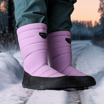 Vaistoa Kinos – lasten korkeavartiset paljasjalkakengät talveen, väri lila. Käyttökuva: etuviistosta kuvattuna lumisella tiellä sinisten housujen kanssa.