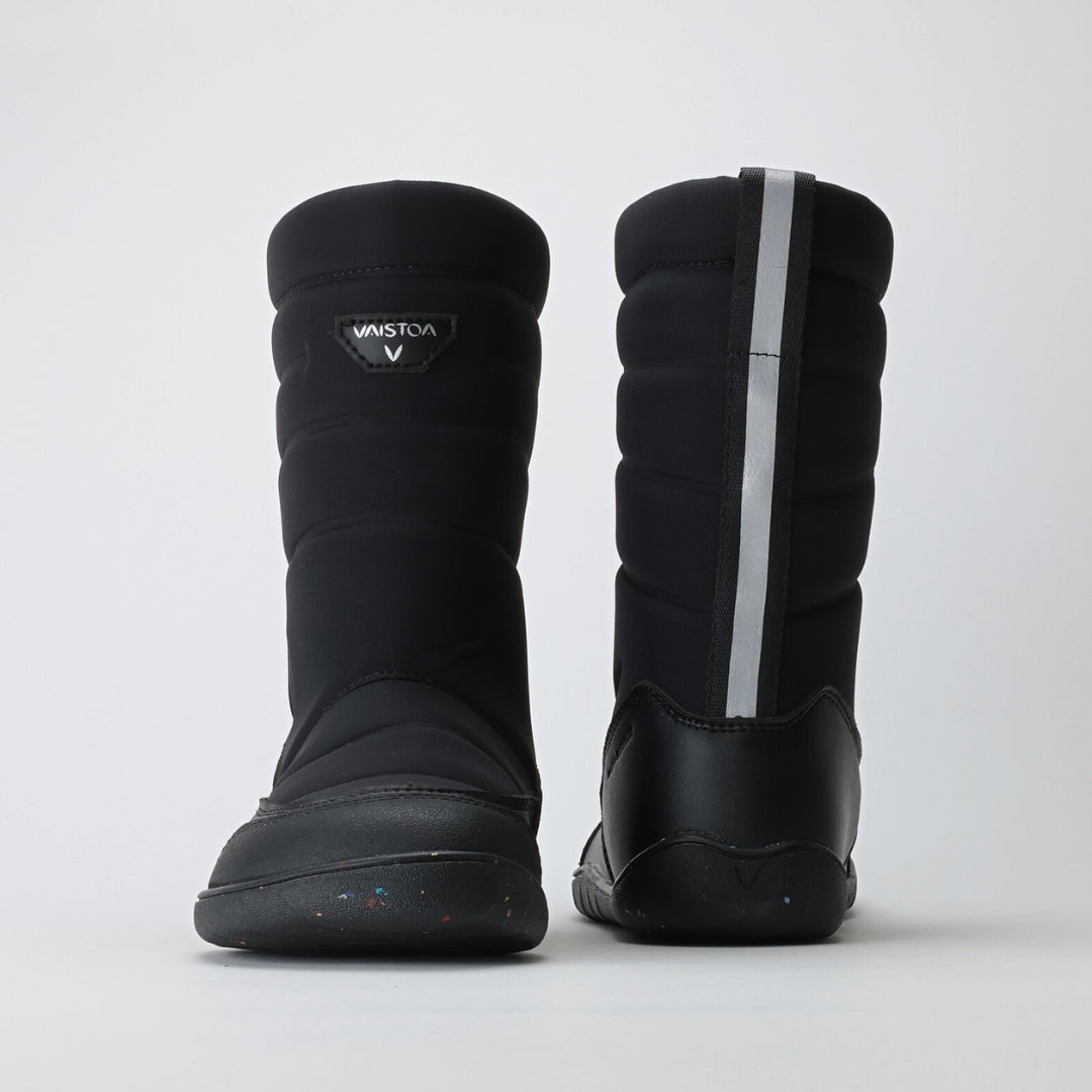 Vaistoa Kinos – lasten korkeavartiset paljasjalkakengät talveen, väri musta. Kuvassa edessä ja takana heijastava nauha, joka lisää näkyvyyttä ja turvallisuutta pimeässä.