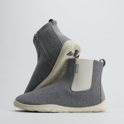 Kaksi helmenharmaata Vaistoa Sulo -huopanilkkuria seisovat vierekkäin valkoisella taustalla. Toinen kenkä nojaa toisen varteen, paljastaen joustavan Vaistoa Pitoa™ -talvipohjan ja minimalistisen muotoilun. Kuvan oikeassa yläkulmassa näkyy Design from Finland -merkki, joka kertoo kotimaisesta suunnittelusta.