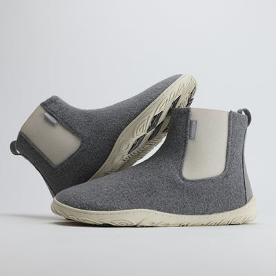 Kaksi helmenharmaata Vaistoa Sulo -huopanilkkuria, joista toinen nojaa toisen varteen. Kuvassa näkyy kengän sivuprofiili ja pohjan kitkapalat, jotka on suunniteltu tarjoamaan varmuutta liukkaalla alustalla.