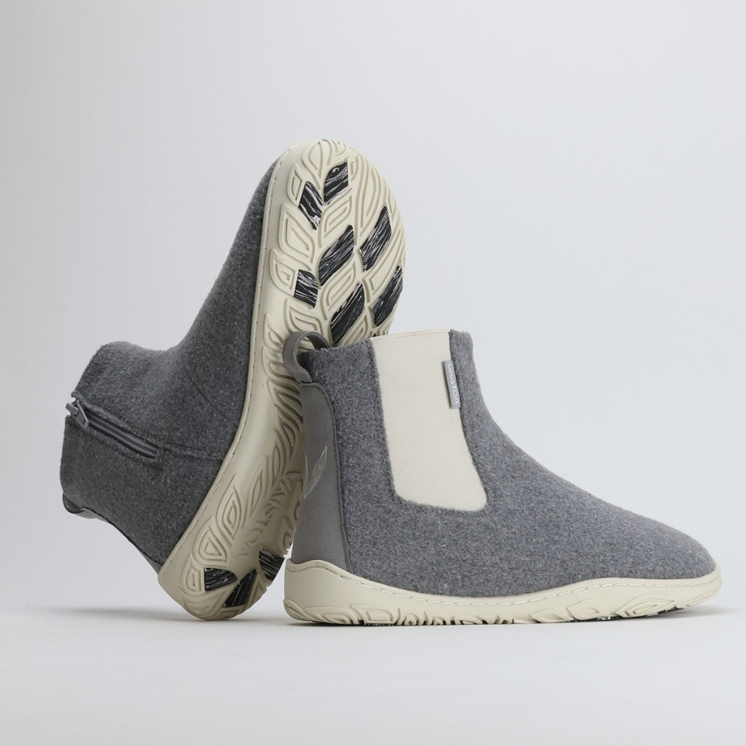 Kaksi helmenharmaata Vaistoa Sulo -huopanilkkuria nojaavat toisiinsa siten, että kengän pohjan kuviointi ja kitkapalat ovat selkeästi näkyvillä. Kuva tuo esiin Vaistoa Pitoa™ -talvipohjan pitävän ja kevyen rakenteen.